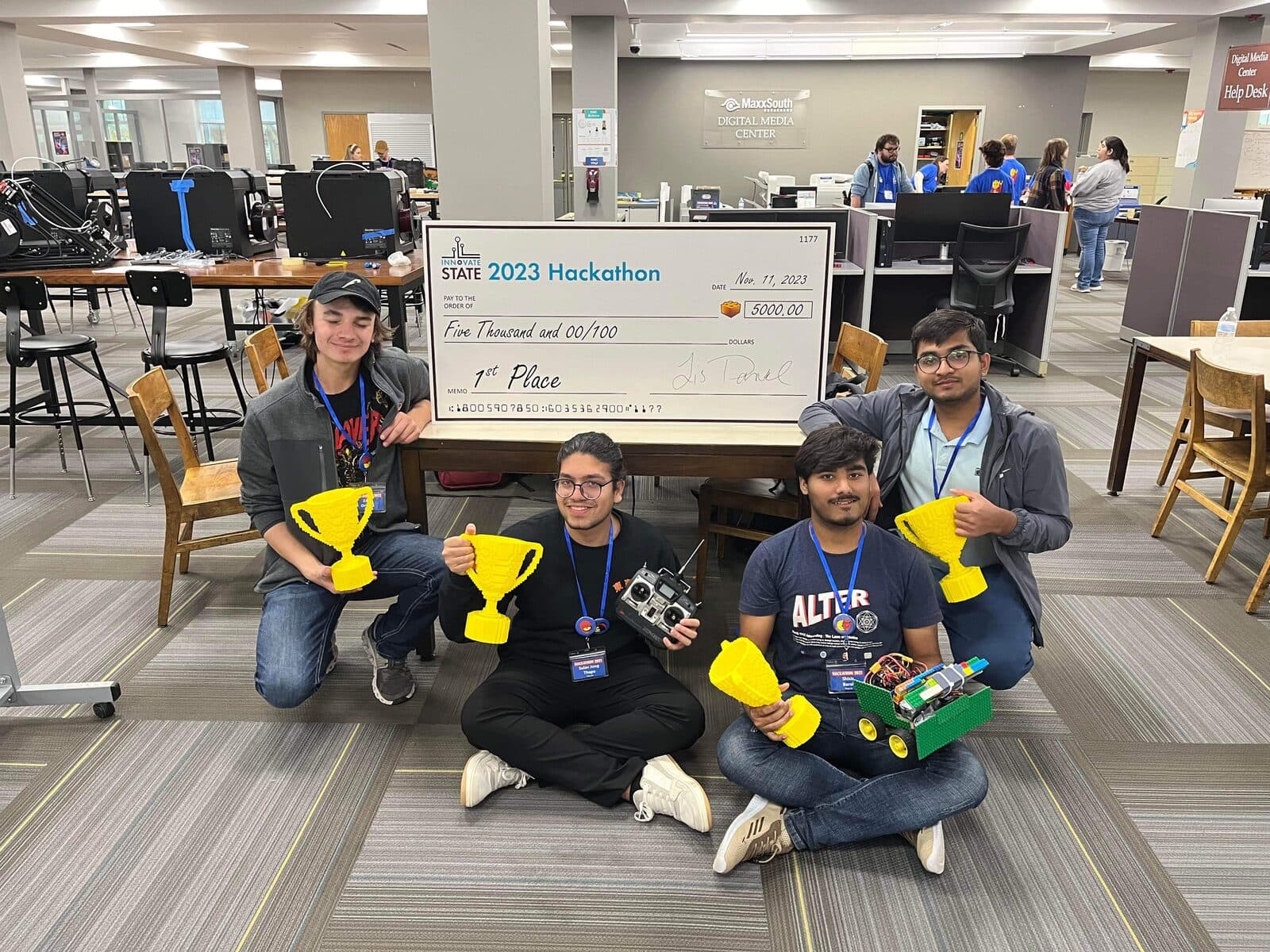 Four teammates with LEGO trophies and a giant first place check at Innovate State 2023